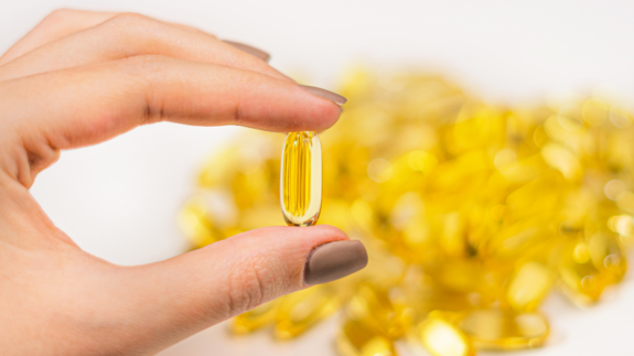 A woman holds a golden capsule in front a pile of vitamins.