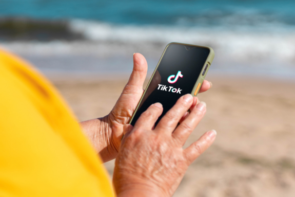 A woman looks at TikTok on her phone while at the beach.